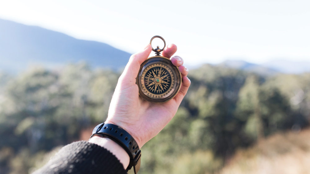 a hand reaching out holding a compass