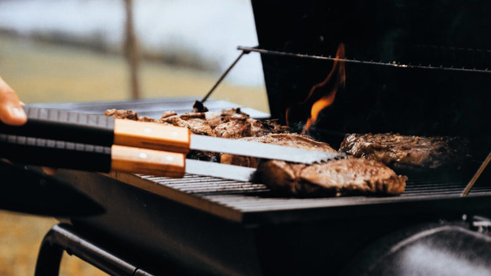 tongs flipping hamburgers on a grill