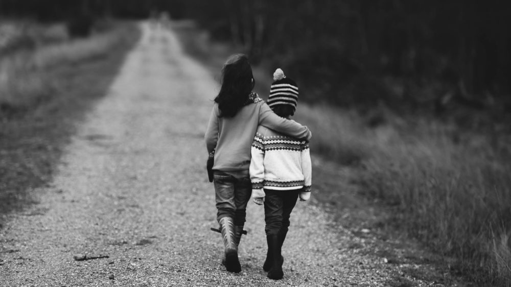 black and white photo of two girls walking down a road with their arms around each other