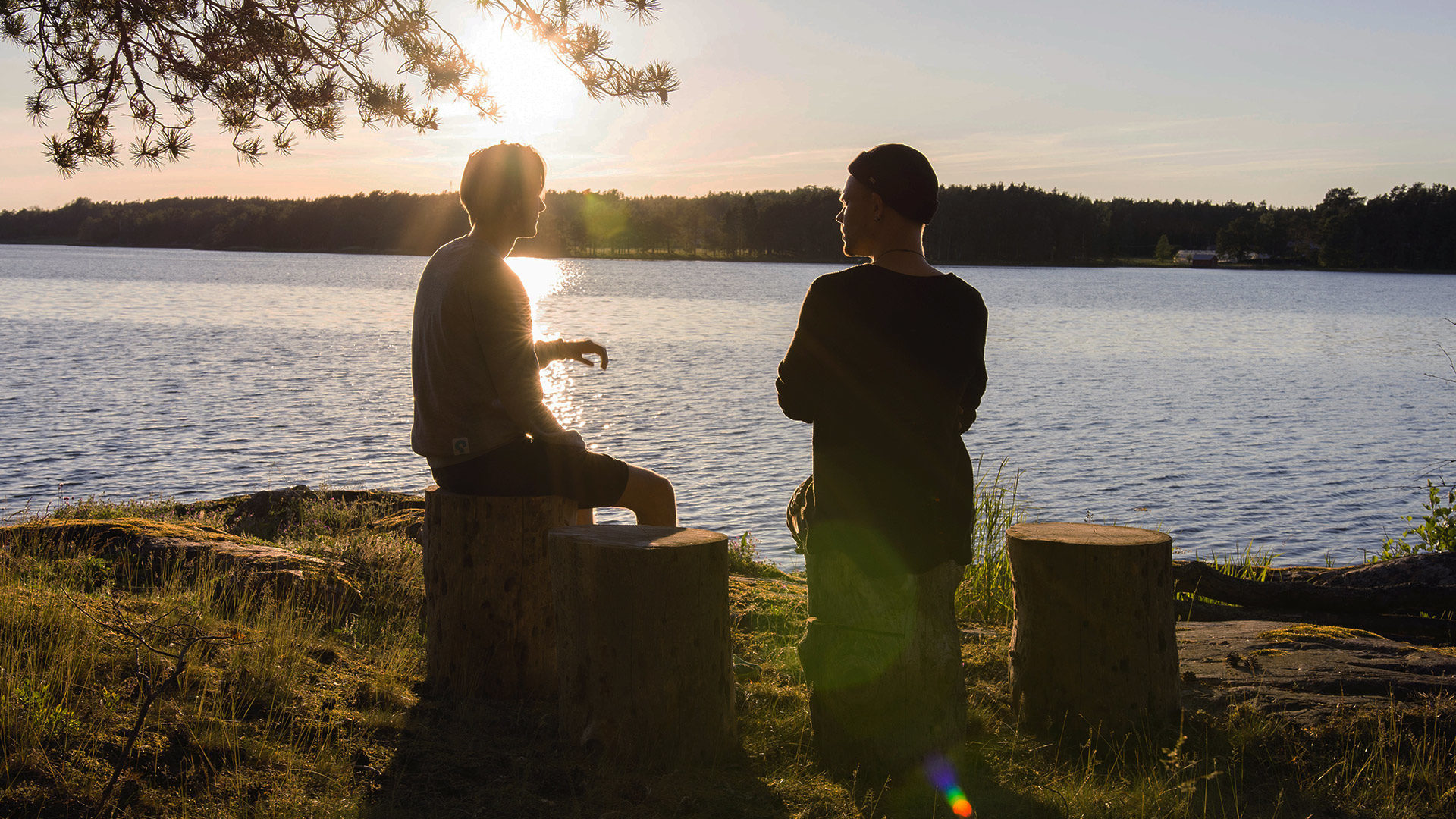 two people sitting and facing each other in front of a lake